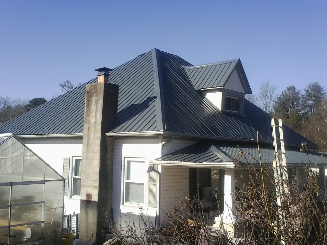 Dark blue standing seam metal roof on a white farmhouse with dormer — Slate & Tile Roof Repair by Roofing Brothers in Cobb