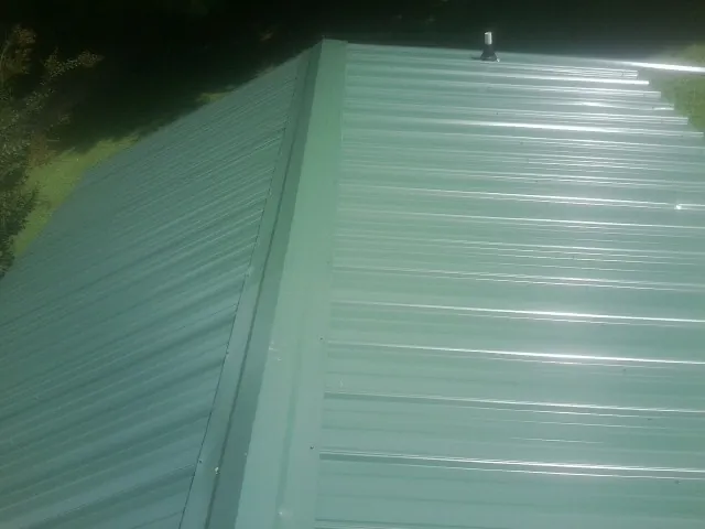 New green metal panels meeting at the ridge of a roof — Flat Roof Repair work by our crew in Cobb