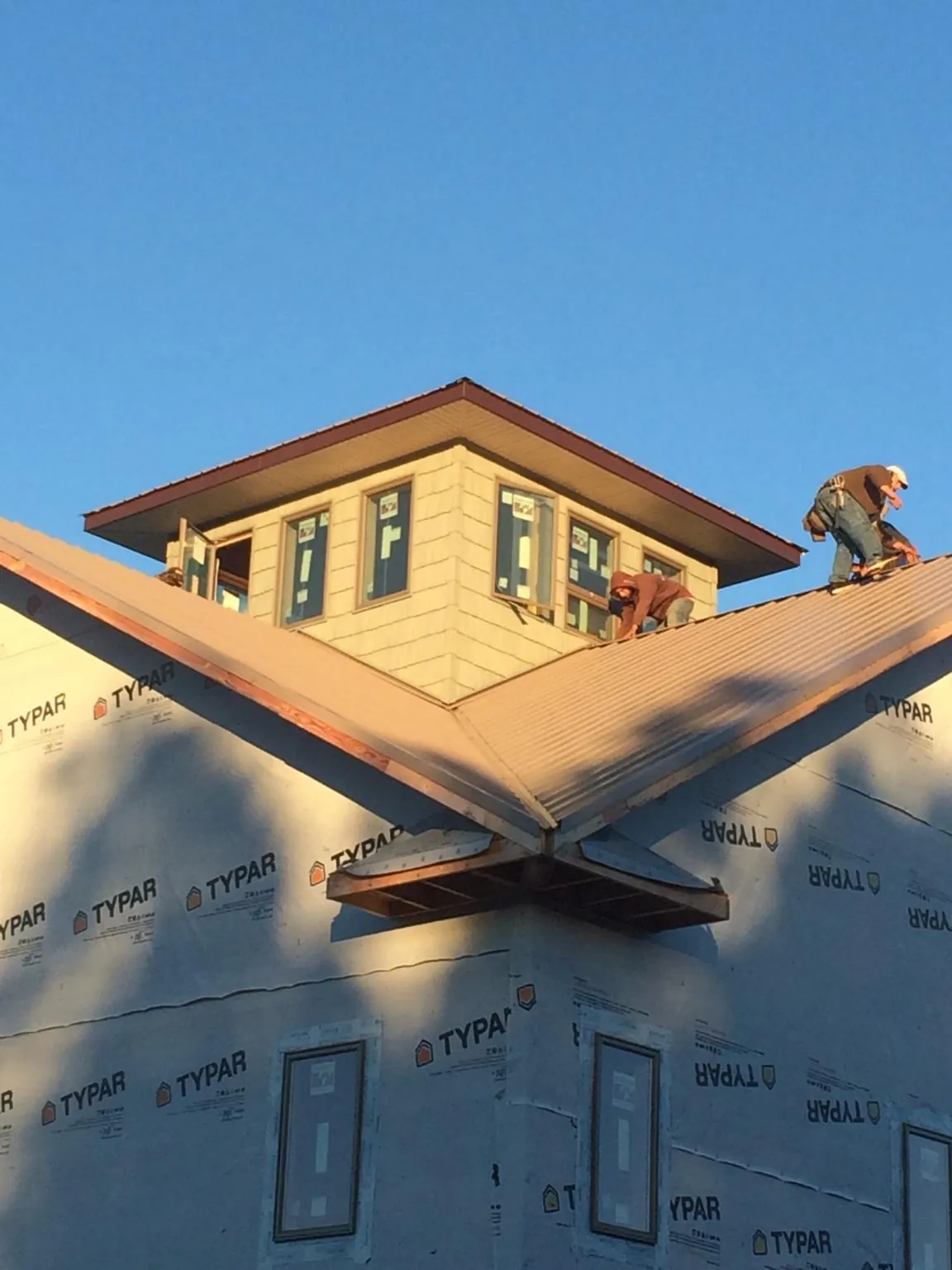 Roofers working around a rooftop cupola on a new metal roof at sunset — Roof Waterproofing in Cobb by Roofing Brothers